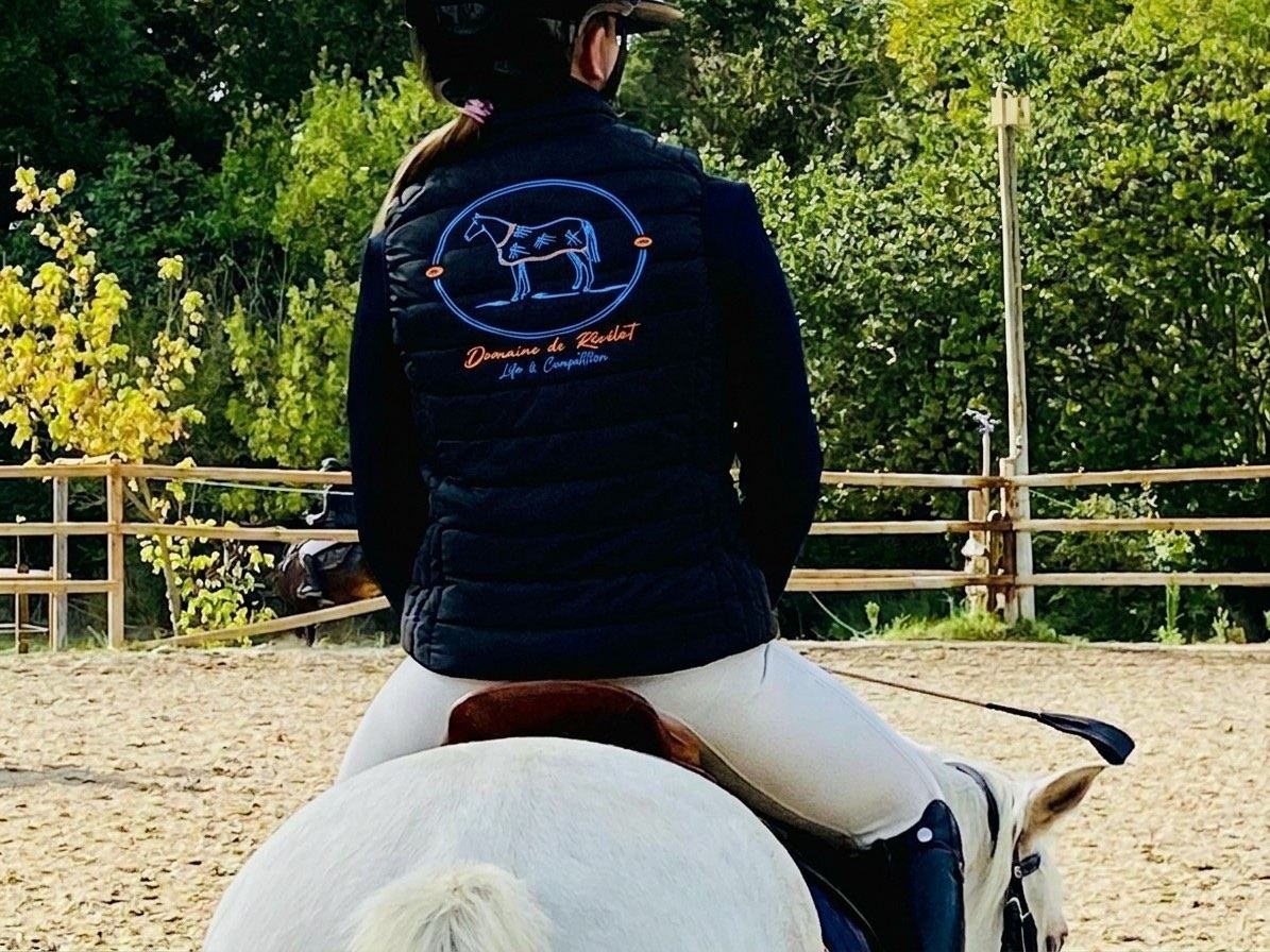 Cavalière de dos portant la doudoune au logo du Domaine de Révélat